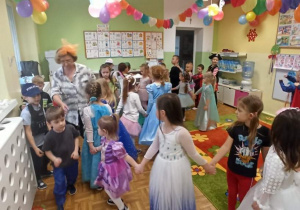 Dzieci w udekorowanej sali tańczą trzymając się za ręce.